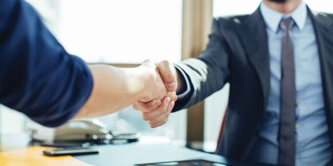 two-people-shaking-hands-over-a-desk-2000×1000